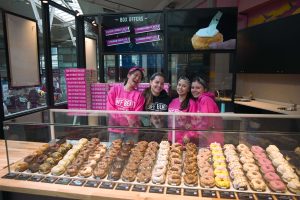 Off Beat Donut Co. team smiling behind a display of colorful artisan donuts at Connolly Station in Dublin, showcasing a wide selection of fresh donuts in a busy train station café